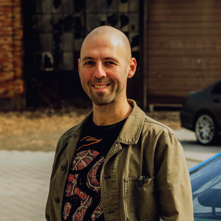 Man standing outdoors with a car and building in the background