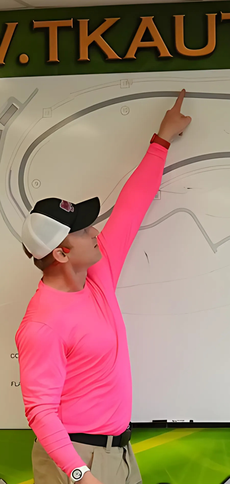 Man in pink shirt pointing to motorsport board